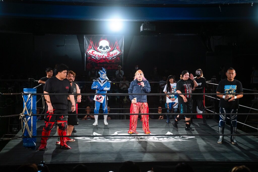 The ring at Shinjuku FACE on 27 July 2025. Mototsugu Shimizu holds the microphone in the centre among the wrestlers.